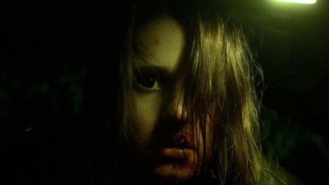 Another still from the film. Isobel Skinner is dimly lit, with blood surrounding her mouth and her hair strewn across her face.