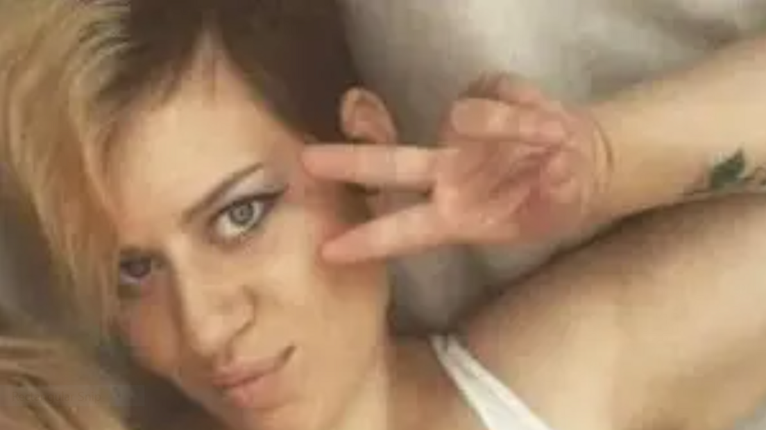 An old photo of Holly Goodchild, with short blonde and dark hair with a fringe. She is wearing make-up doing a peace sign, while looking into the camera.