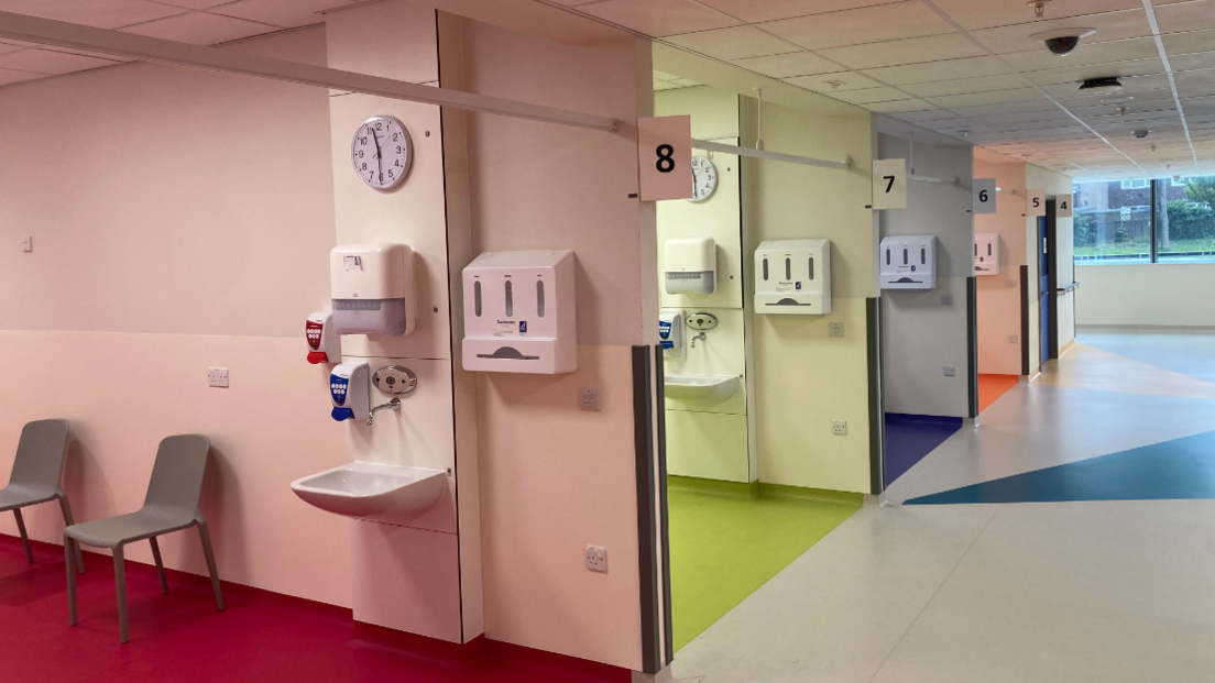 A series of beds in a hospital ward, each with different coloured, pastel walls