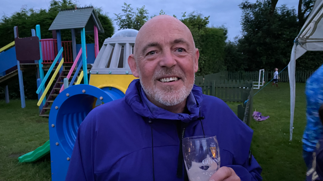 Steve Godwin, wearing a blue waterproof jacket and holding a half finished pint