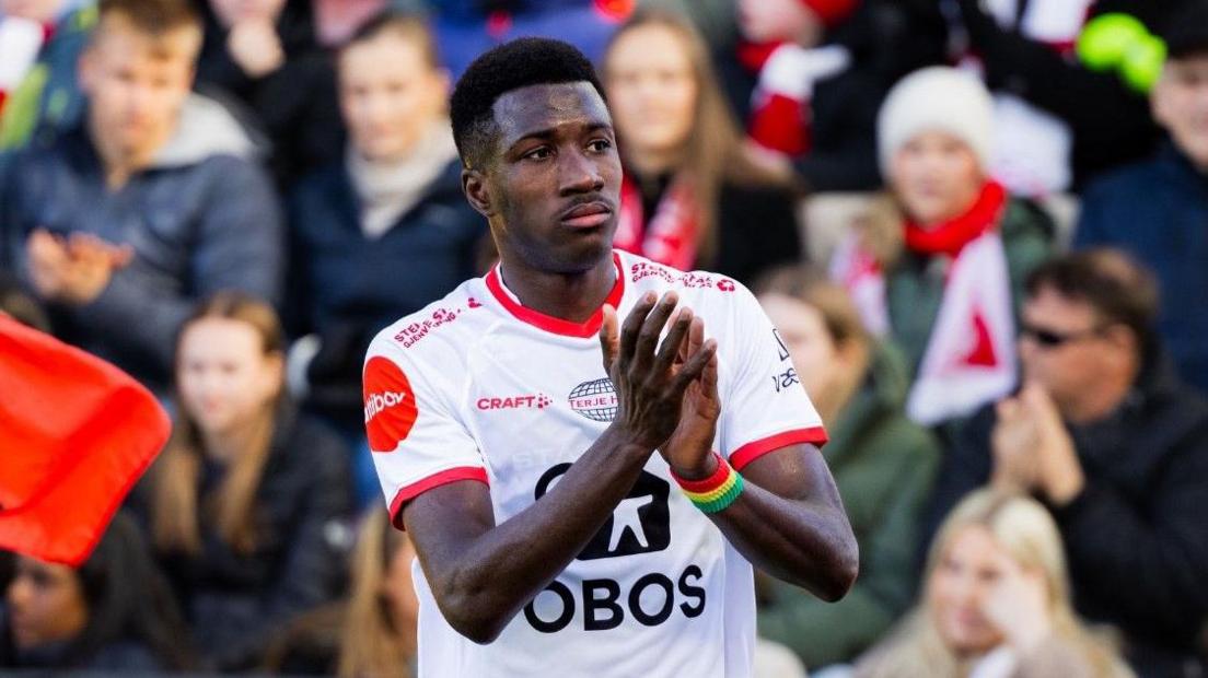 Mai Traore pictured applauding during a match, with a crowd in the background