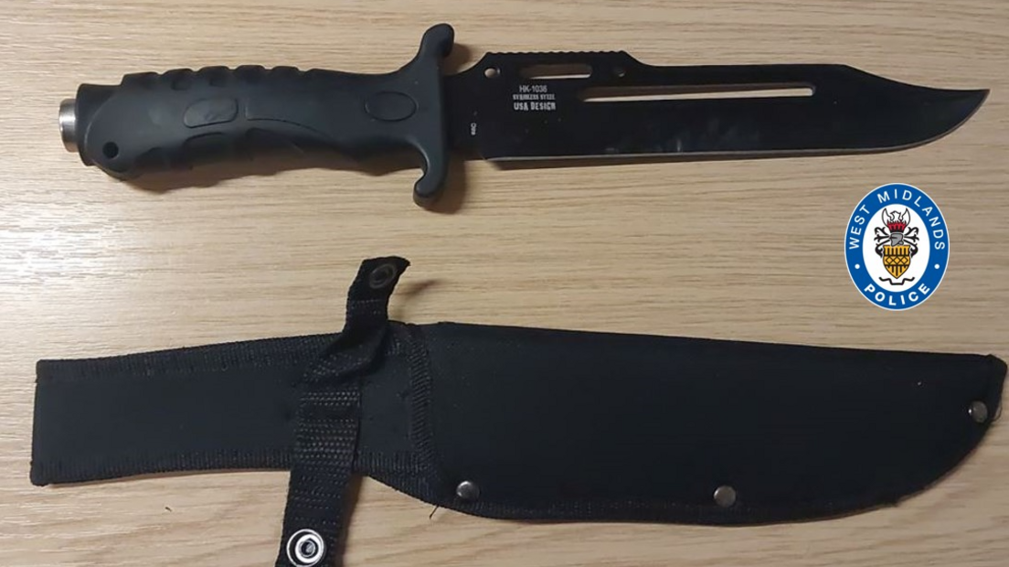 A black knife on a table alongside its sheath