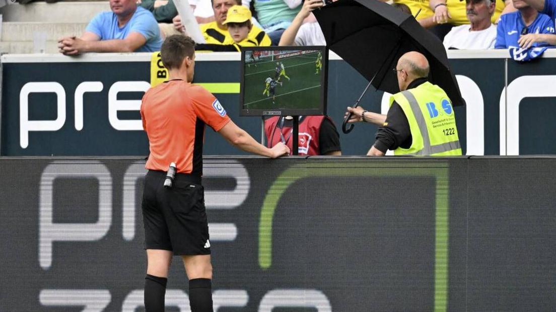 A referee examines a VAR monitor pitchside which is showing a replay