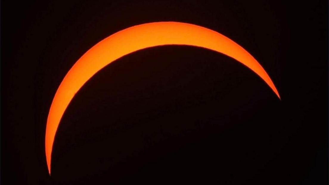 An orange semi-circle view of the sun in an otherwise black sky.