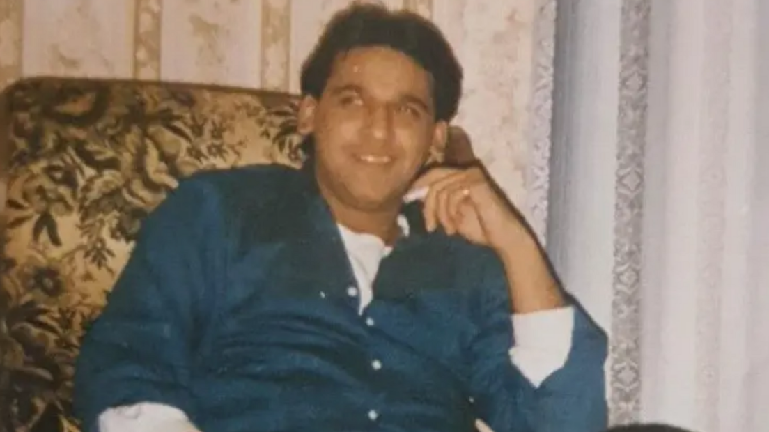 Shami wearing a blue shirt with white buttons and a white top underneath. He is sitting on a patterned arm chair