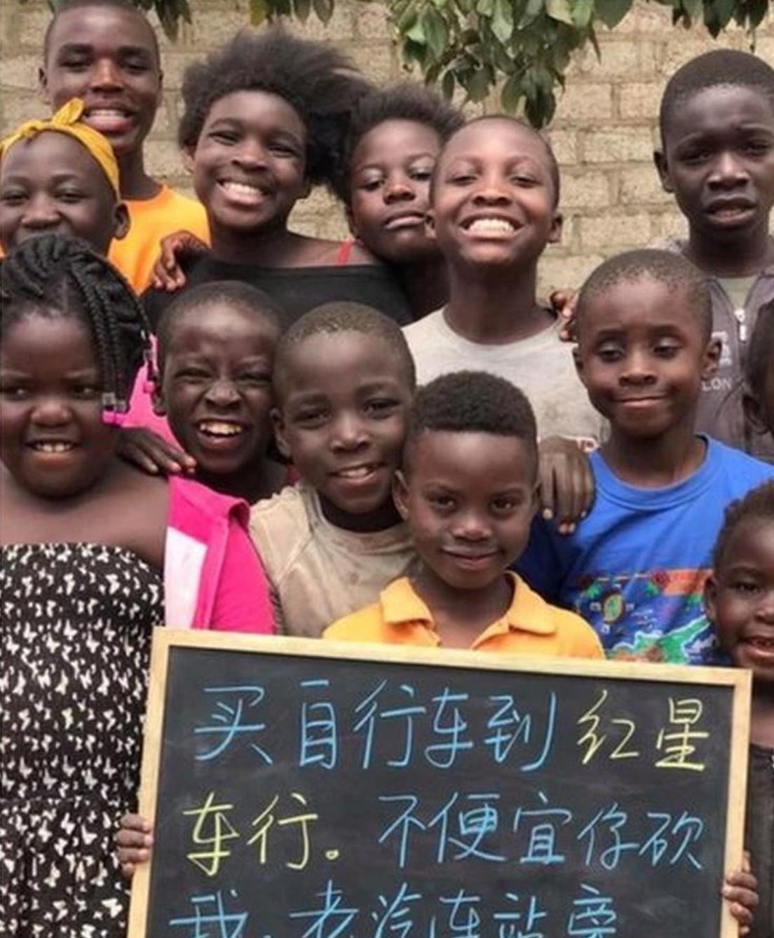 Children pose for a group picture behind a black board.