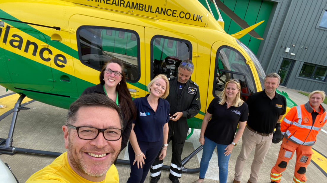 Mike is with a crew from Wiltshire and Bath Air Ambulance, all standing in front of their helicopter which is bright yellow. All are smiling at the camera.