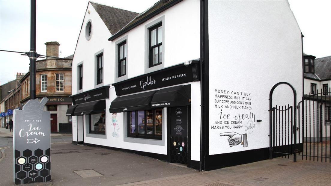An ice cream and chocolate gift shop, with white and black walls and doors. A sign advertising ice cream sits outside it.