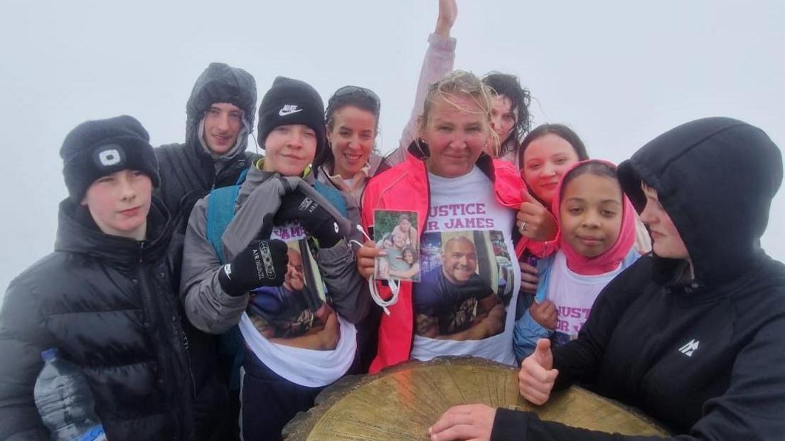 Adele Cook, alongside friends and family, on the top of Snowdon with a photo of James in her hands.