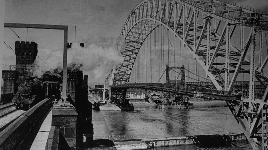 The distinctive metal structure of Runcorn bridge in the early 1960s alongside a steam train