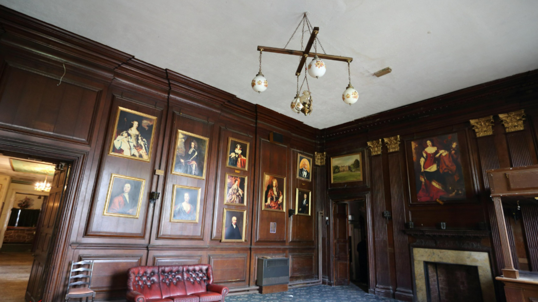 A panelled room inside Woolton Hall, with paintings on the walls, and a red leather sofa beneath some of them.