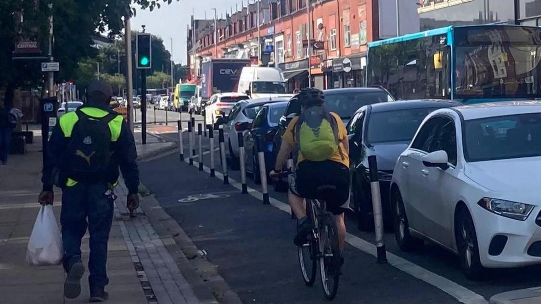 A cyclist using the Linthorpe Road Cycleway. There are cars and buses on the road besides the cyclist. 