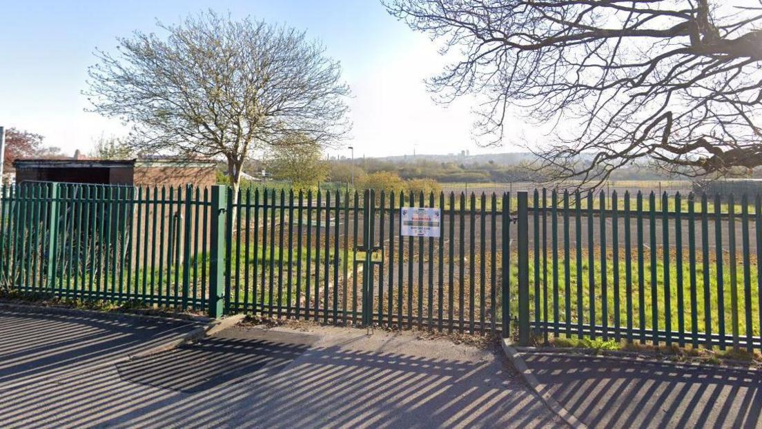 A street view of the vacant former school site, fenced off on Butterworth Road in Oldham on a sunny day.