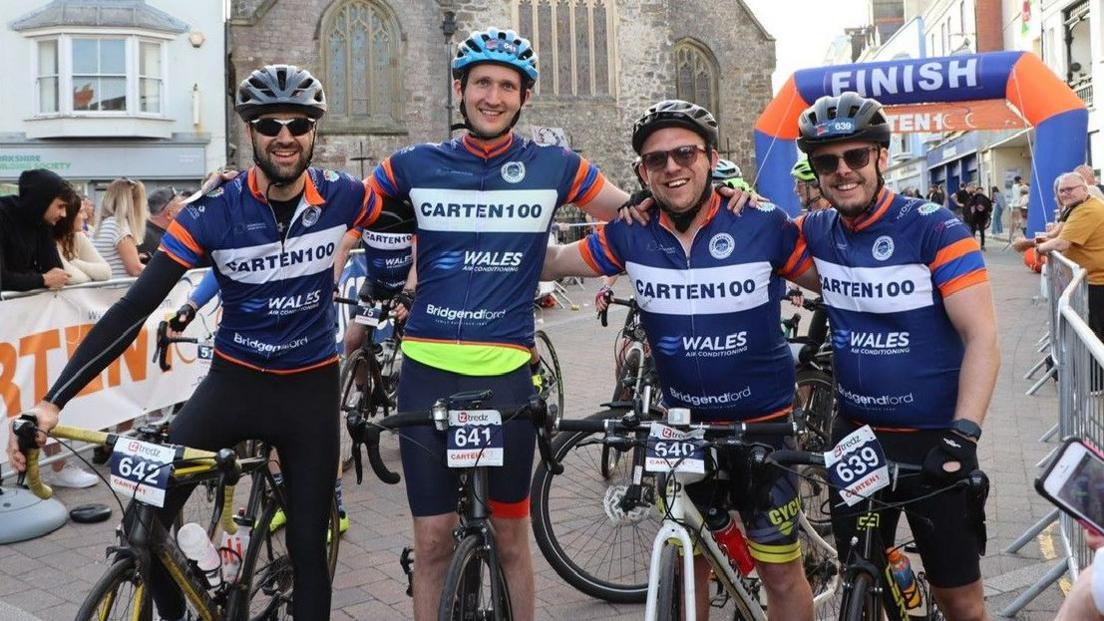 Four cyclists smiling arm in arm after crossing a finish line