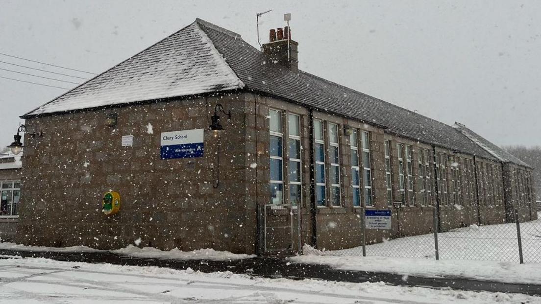 Snow is falling in this chilly scene at Cluny School. The school is building is of a Victorian design. There is snow on the ground around it.