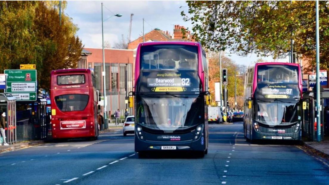 Two double decker buses facing towards the screen with another facing away on a main road in Birmingham