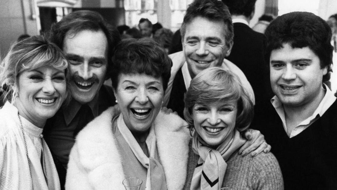 A black and white image of six people filling the photo and mainly looking at the camera.