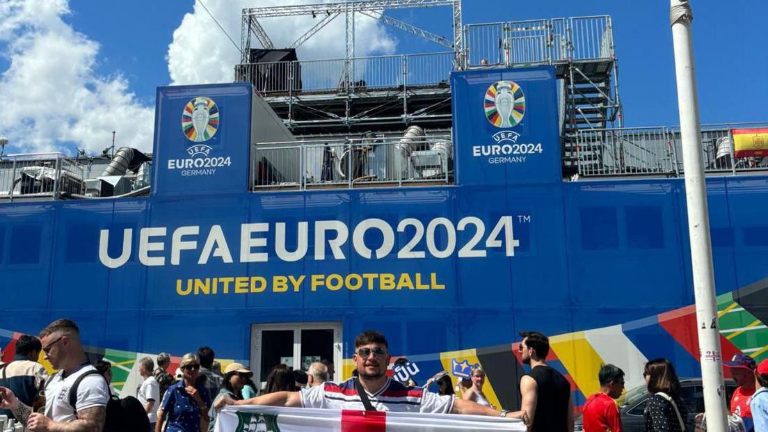 Casey Bishop stood outside a book stadium with the words 'UEFA Euro 2024, united by football' written in white letters. 