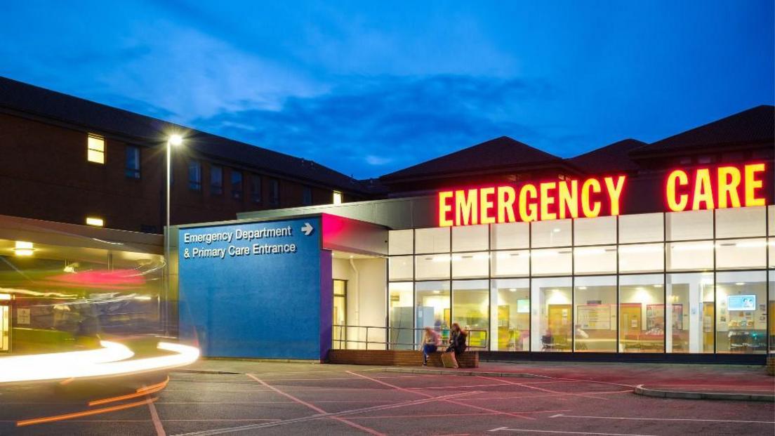 The Emergency Department of the hospital at night, with a lit up sign saying EMERGENCY CARE