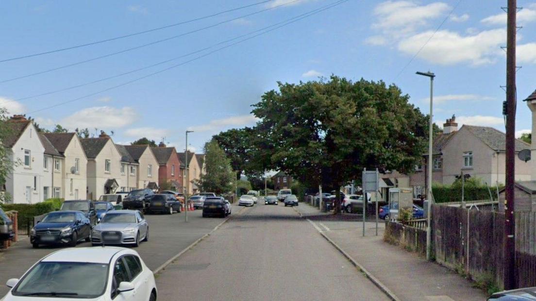 A still of Bibury Road in Gloucester, a residential road with cars parked on the left