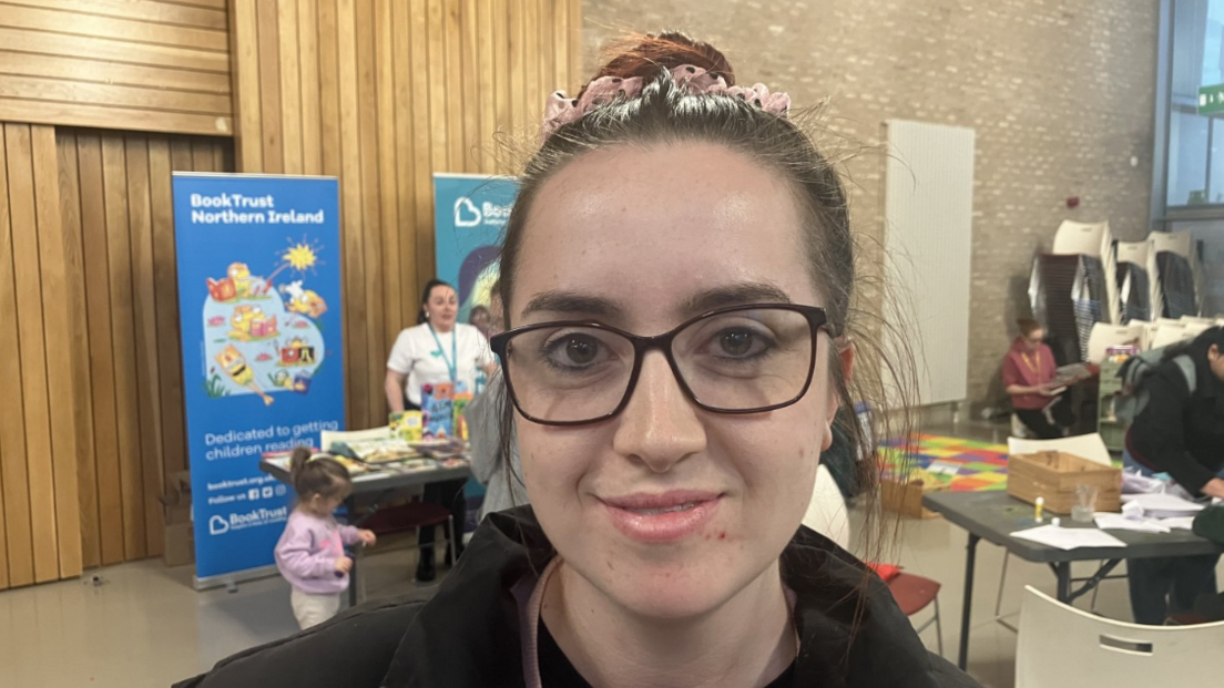 Jessica Gilmore with glasses and pink bow in hair in front of signs and stalls