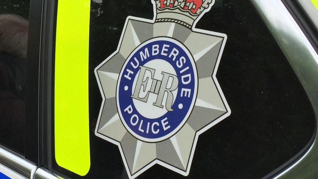 The side of a Humberside Police car zoomed in on the Humberside Police logo which is written in a circle surrounding a silver star and crown.