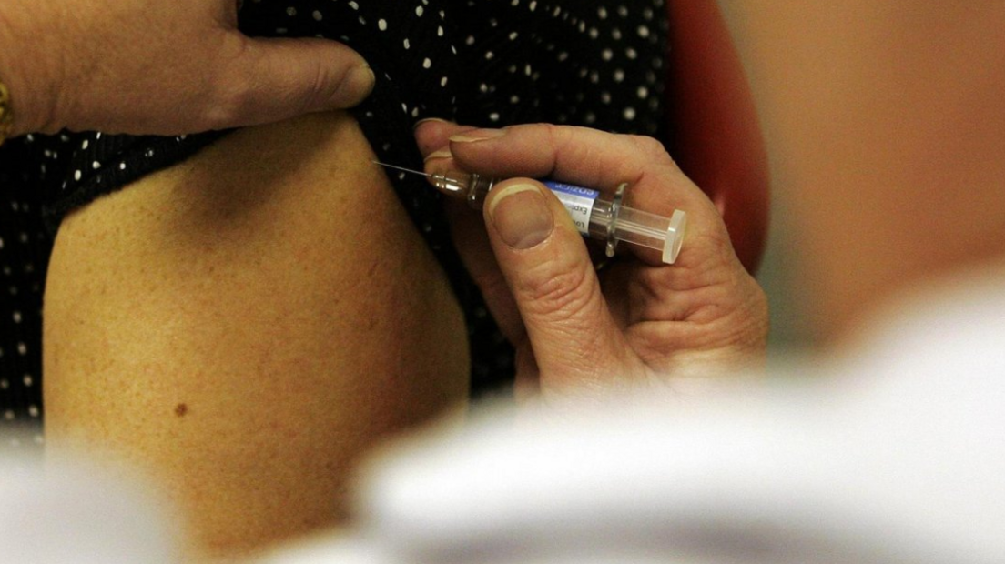 A close-up of a syringe being pushed into someone's arm. Neither person can be identified
