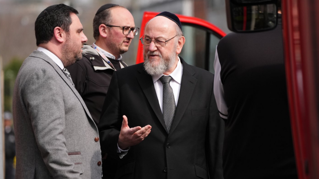 Kryerabini Sir Ephraim Mirvis zbret nga një automjet dhe i flet një burri me kostum gri.
