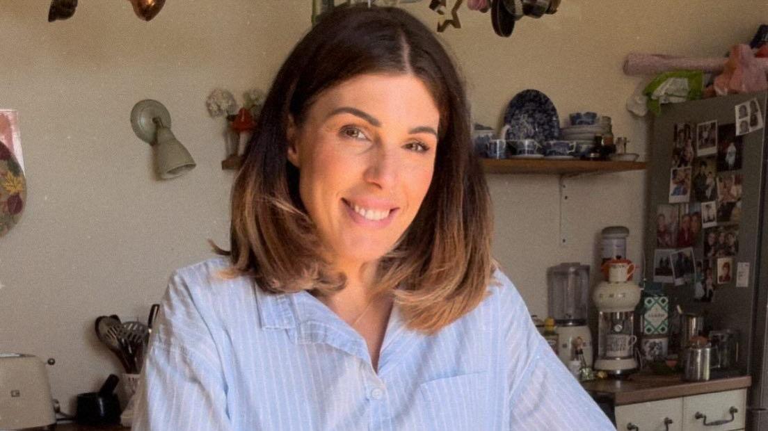 A dark-haired woman wearing a blue striped top, leaning over a kitchen table.