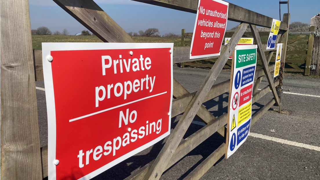 Signs on the wooden gate at Oakwood. One is a red sign which in white font reads "Private property - No trespassing"