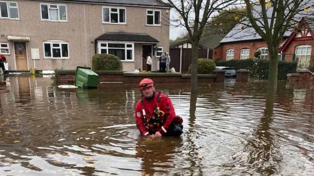 A man in red overalls standing waist deep in water in front of a row of houses