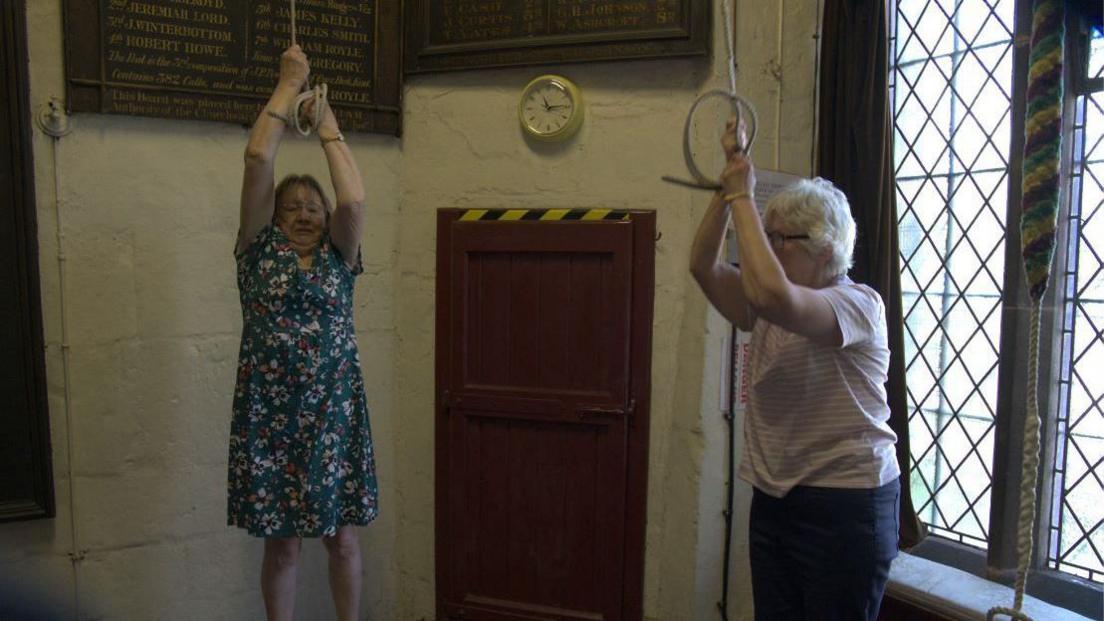 Two women pull the bellringing ropes inside a church