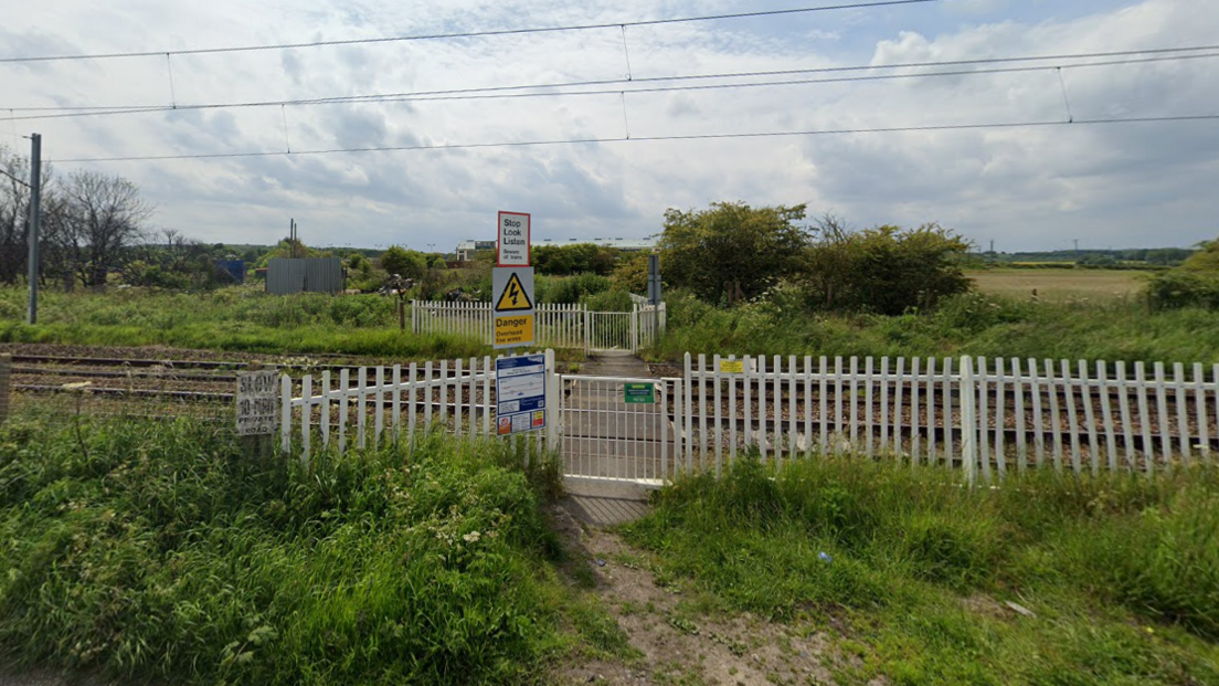 White gates and greenery in front of a rail line