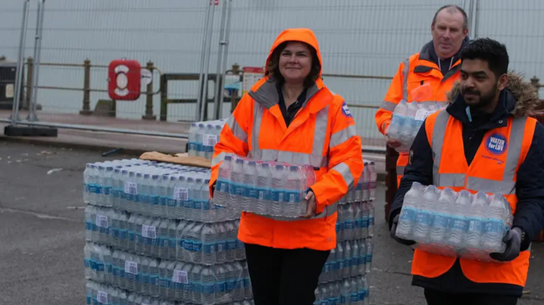 Staff in high vis carrying large plastic bottles of water at a water station in Hastings on the seafront