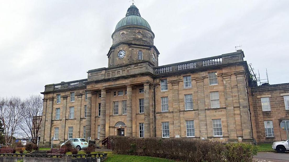 An exterior shot of dr gray's on a grey cloudy day. the sandstone building with four columns rises up to a copper dome above an old clock face.