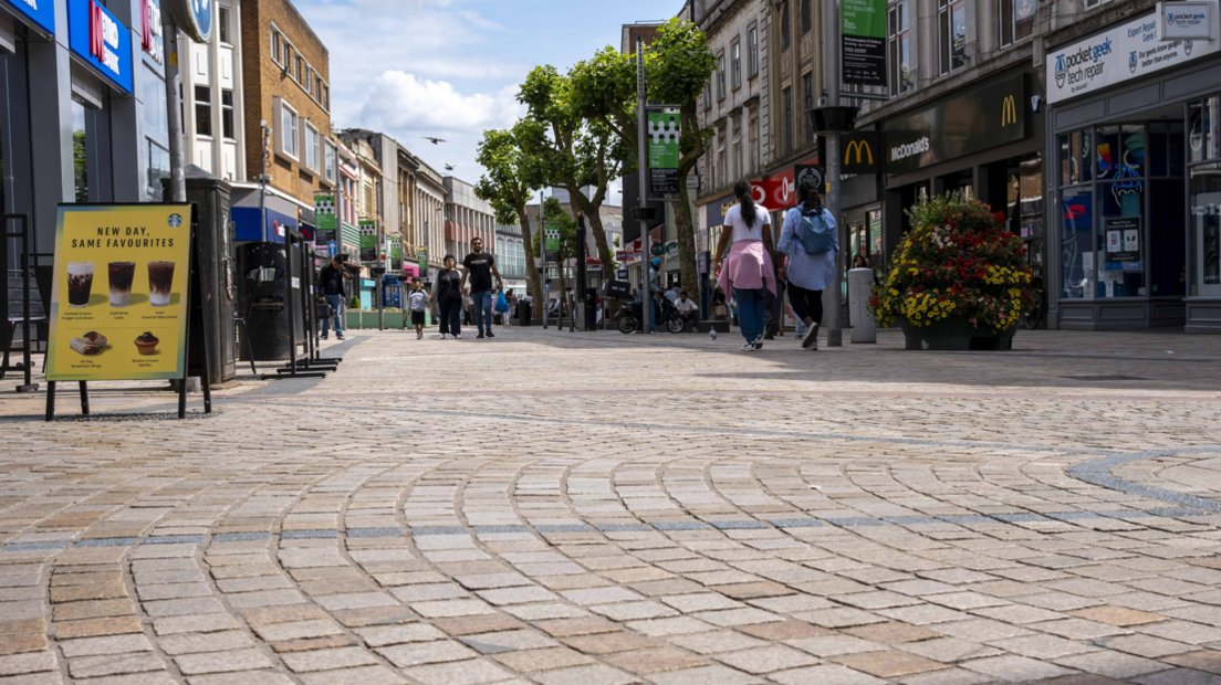 New paving in Wolverhampton city centre is bathed in sunshine with a number of shoppers walking past shops on both sides