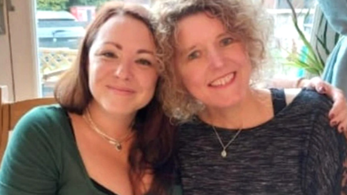 Helen and Rachael side by side smiling with their heads close together, with Helen's arm around Rachael's shoulder. One has curly blonde hair, and the other long dark hair. 