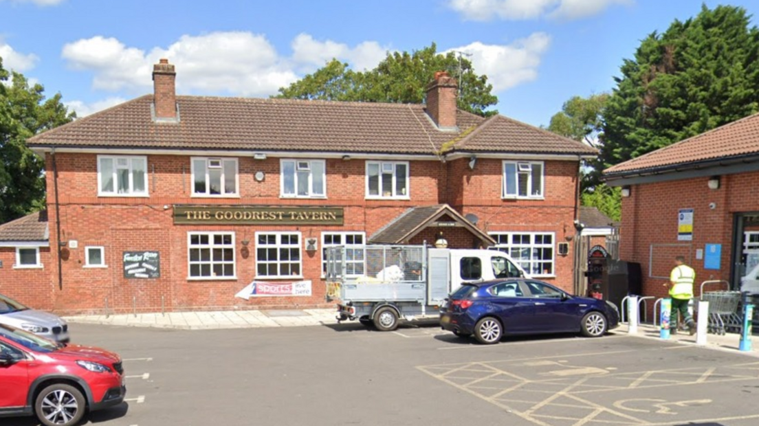 A pub car park with a large building with the words The Goodrest Tavern in gold lettering on a green sign