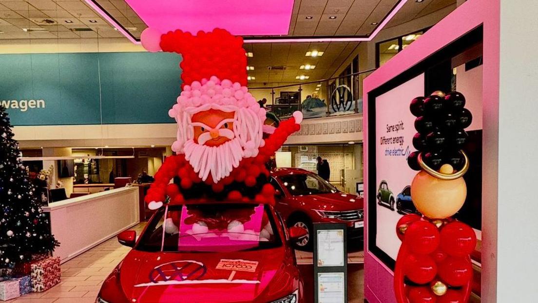 A red car with a large Father Christmas made entirely from balloons seated in it