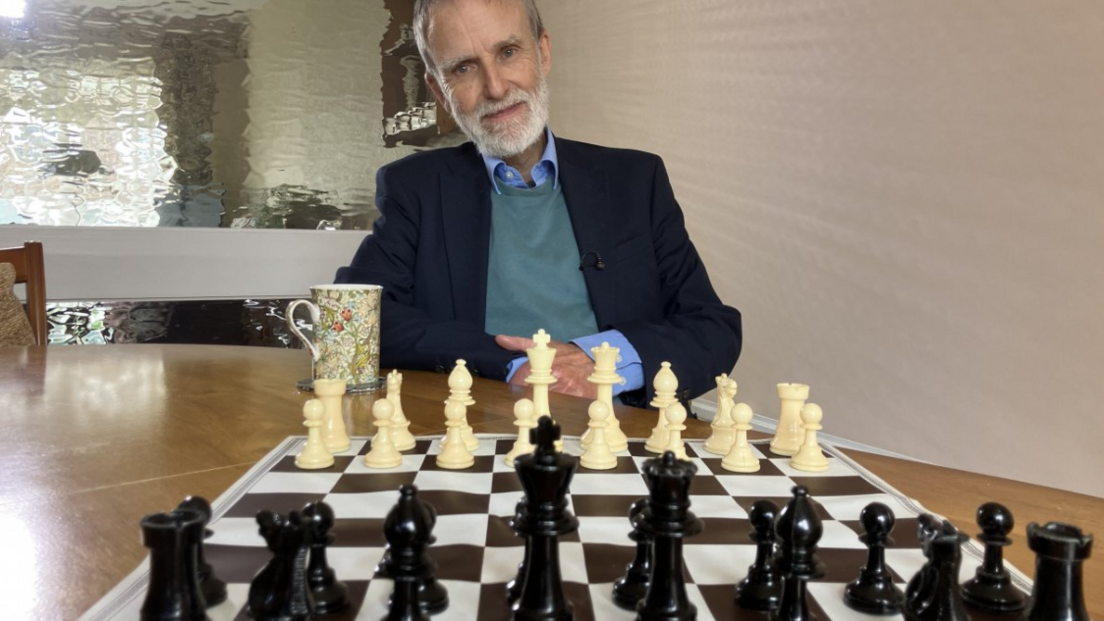 A man smiling to camera with a chess board laid out in front of him at the beginning of a game.