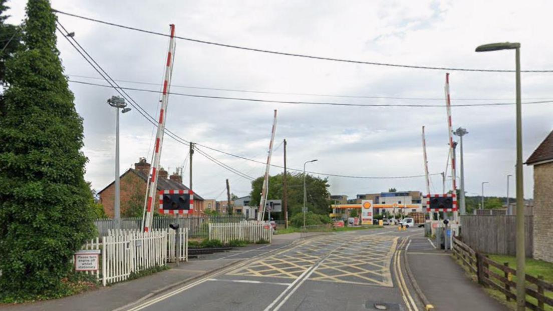 A google maps screenshot of the london road rail crossing. It is on a single carriageway, and has four separate barriers, as well as lights. Further down the road is a petrol station.