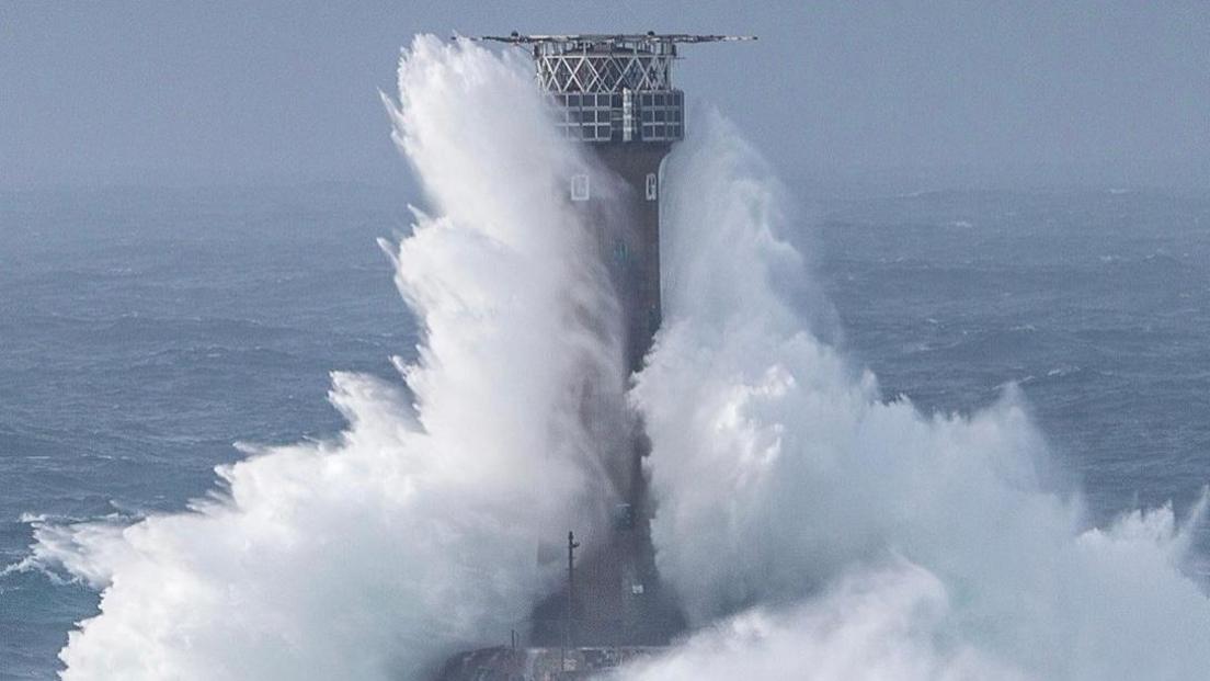 A wave hits a lighthouse off the coast.