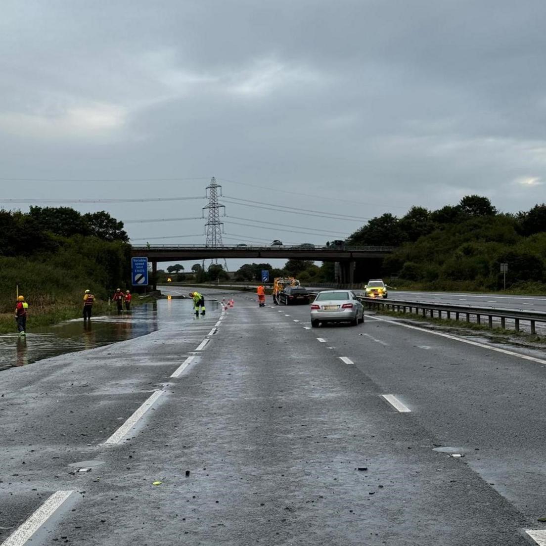 A view of the M5 with one abandoned car, another being recovered and fire officers on the side with flooding on the route