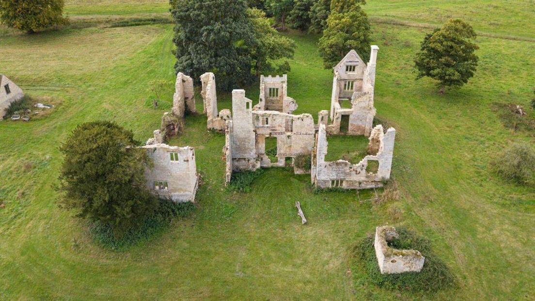 Aerial view of the ruined Elizabethan house at Hampton Gay. Just a few of the stone walls remain, surrounded by grass and trees.