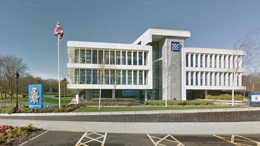 View of Aykley Heads, the headquarters of Durham Police - a two storey concrete and glass building featuring a large Durham Police sign to the front of it and a flagpole with a Union Jack.