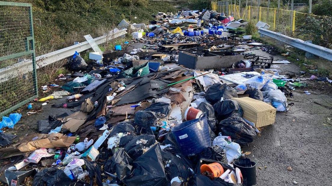 Rubbish dumped on a lane in Bristol. The image shows a variety of discarded items such as bags of rubbish, broken furniture and plastic waste. It stretches for many yards, from just in front of the camera into the distance