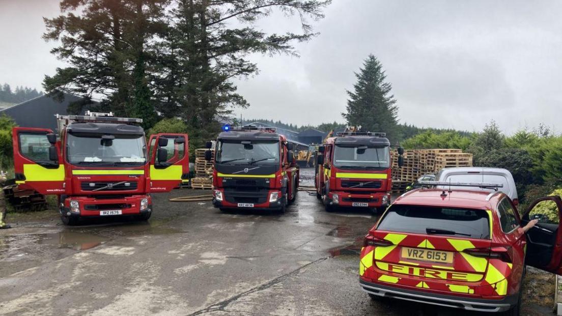 Three fire engines and a fire service car parked on concrete in front of forestry.