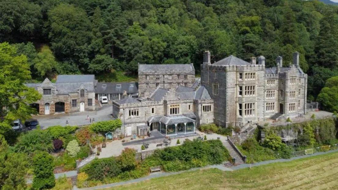 Grand-looking Plas Tan y Bwlch on a hillside with ornamental gardens in front and woodland behind