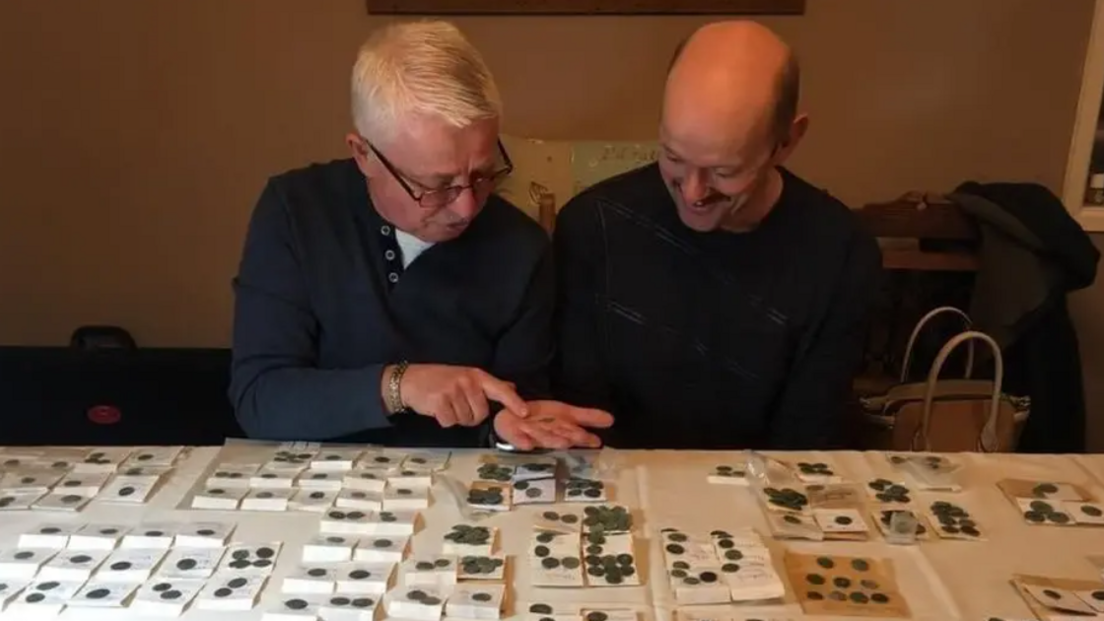 Mr Daw wearing a blue jumper sat at a table looking at cold coins with his friend Martin Fulloway.