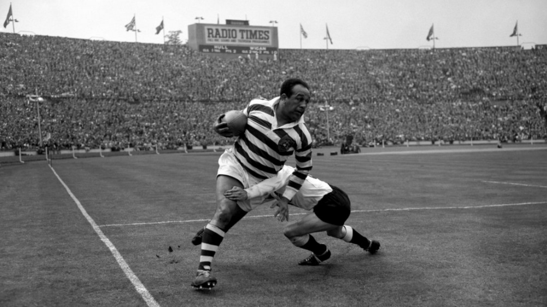 Billy Boston bursting through a tackle at a packed Wembley during the Rugby League Challenge Cup Final in 1959 in a black and white photo